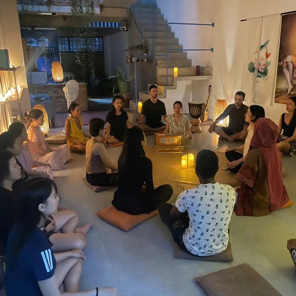 People sitting in a circle on the floor, backs straight, eyes closed.