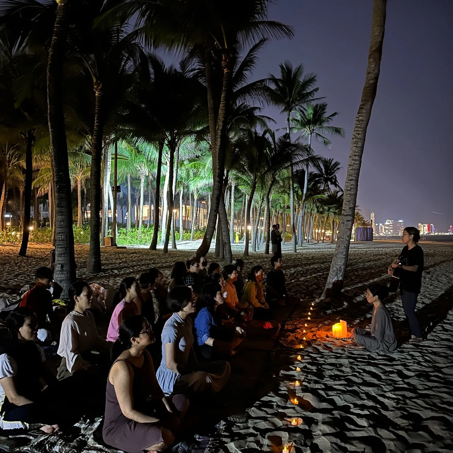 A crowd sitting on the sand around candles in the evening.