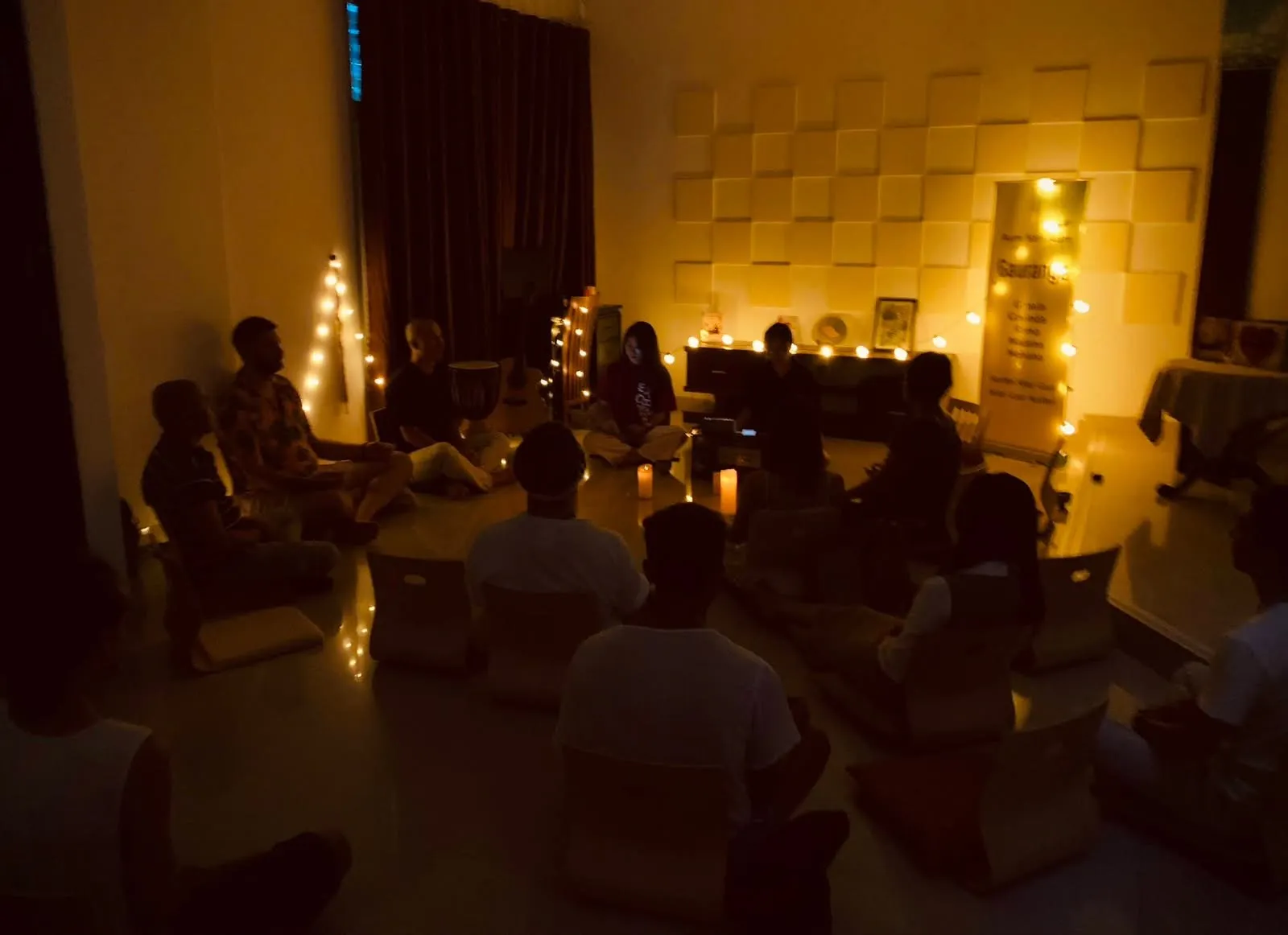 Một vòng tròn người ngồi thiền trong căn phòng tối, chỉ có ánh nến và đèn dây.