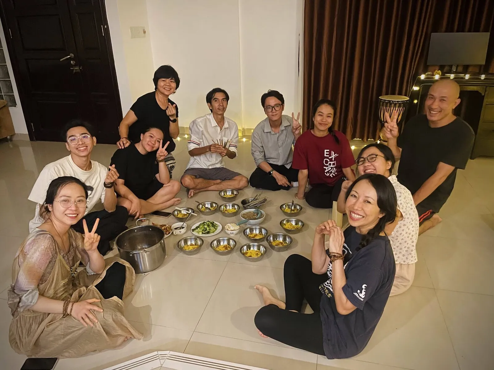 Một nhóm người ngồi dưới sàn quanh những đĩa thức ăn chay, cười vui.
