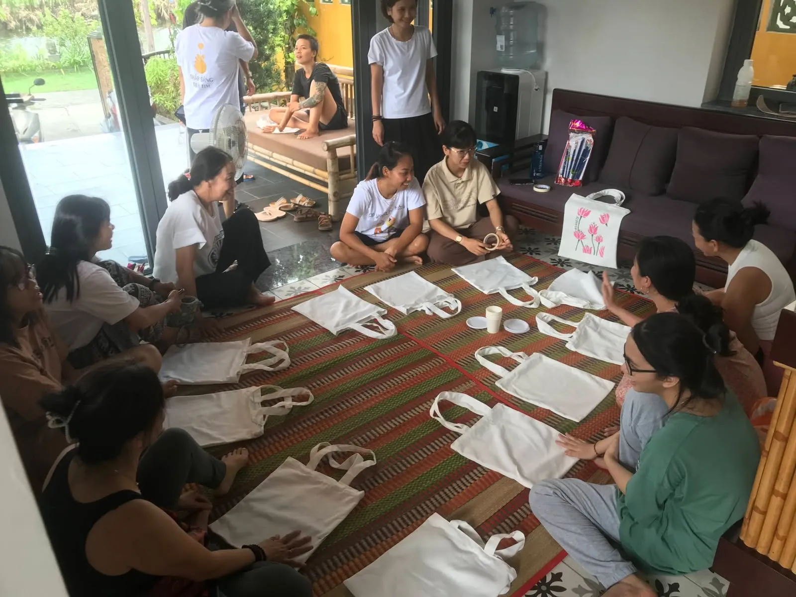 Mọi người ngồi trên chiếu, chuẩn bị vẽ lên những chiếc túi vải trắng.