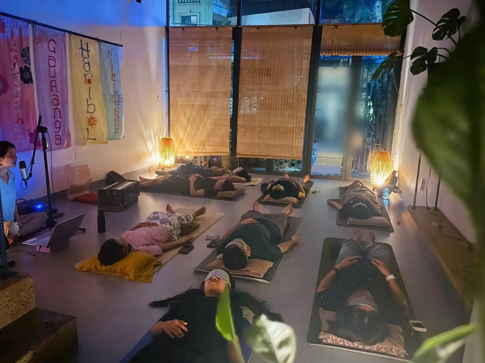 Mọi người nằm thư giãn trên thảm, mắt đeo khăn che, trong căn phòng ánh đèn dịu.